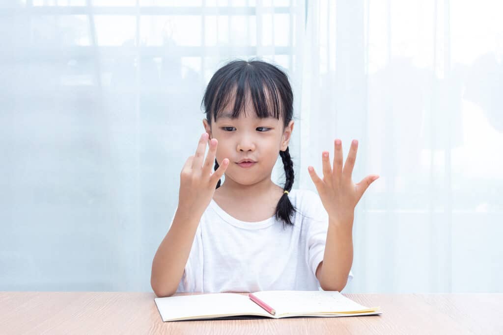 Asian little Chinese Girl doing mathematics by counting fingers at home